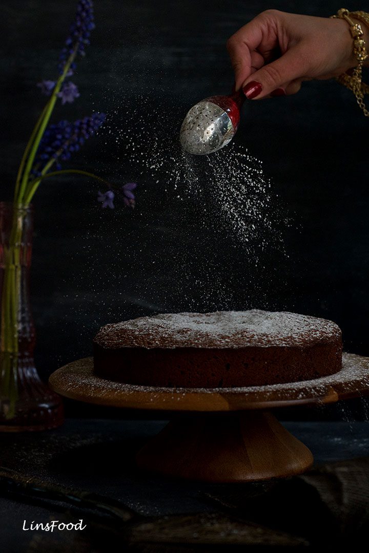 Sprinkling sugar on chocolate cake (torta caprese), dark photo